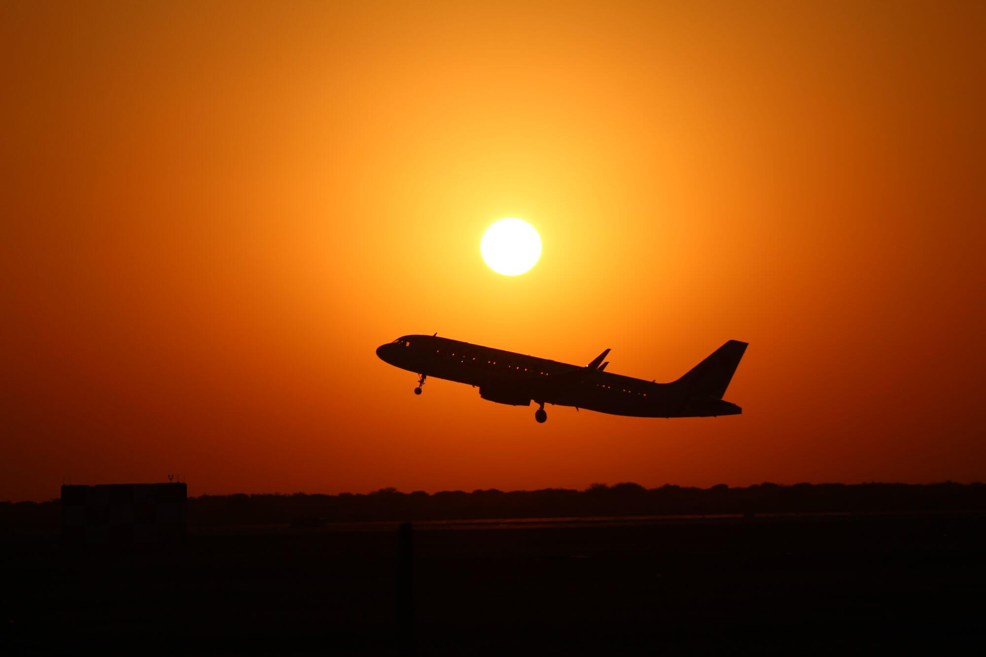 Airplane taking off silhouetted against a sunset